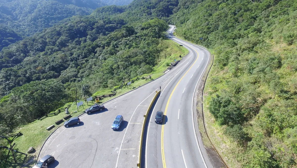 Rodovia de pista dupla cortando área de mata em região serrana
